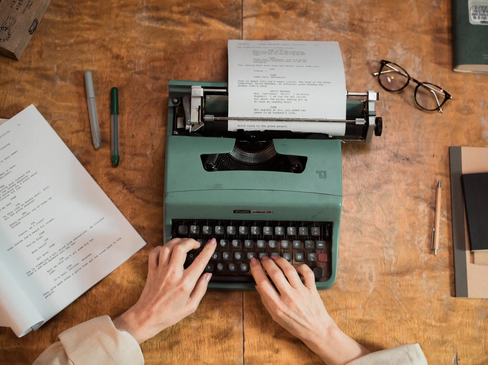 person holding green typewriter on brown wooden table